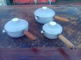 trois casseroles posées sur une table, avec des poignées en bois