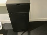 a black trash can sitting in the corner of a bathroom