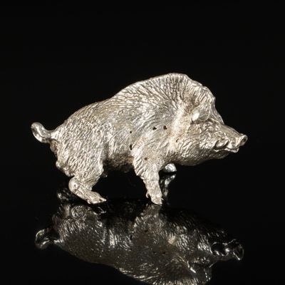 a silver figurine of a boar on a black surface