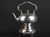 a silver teapot on a stand with a handle