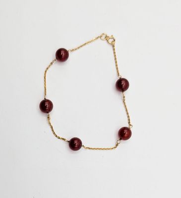 a gold chain bracelet with red glass beads on a white background