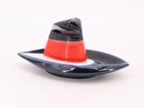 une petite assiette sur laquelle est posé un chapeau, posée sur une surface blanche