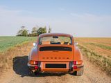 an orange car is parked on a dirt road near a field