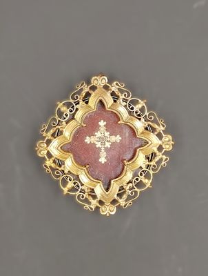 a close up of a gold and red broochle with a cross on it