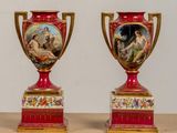pair of red and gold vases with paintings on them sitting on a table