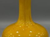 a yellow vase sitting on a table with a gray background