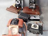 four old cameras sitting on a table with a leather case