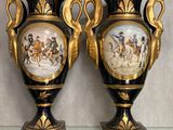 une paire de vases noirs et dorés ornés de peintures, posés sur une table en verre