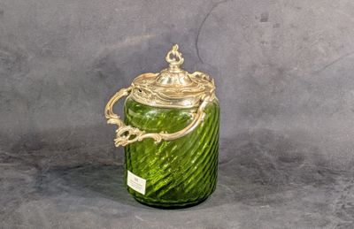 un bocal en verre vert avec un couvercle doré sur fond gris