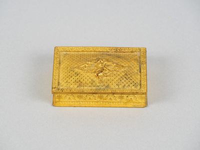 une boîte dorée ornée d'un oiseau, posée sur une surface blanche