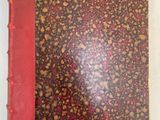 an old book with a red cover sitting on top of a white surface