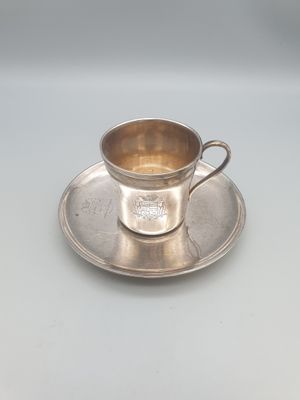 une tasse et une soucoupe en argent posées sur une soucoupe, sur une table