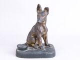 statue en bronze représentant un chien assis sur un rocher, sur fond blanc