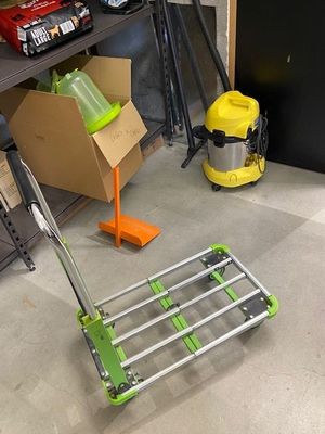 a cart with a green handle sitting on the floor next to a pile of boxes