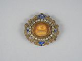 an image of a gold and blue broochle with a picture on it