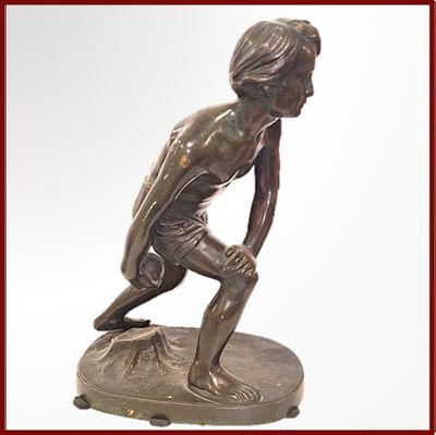 statue en bronze représentant un jeune garçon agenouillé sur un socle, tenant une raquette de tennis
