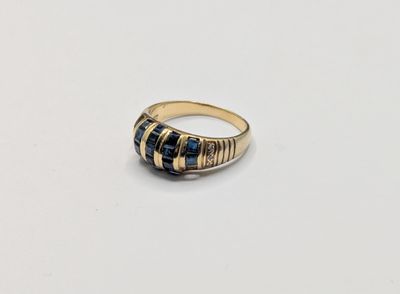 un gros plan d'une bague en or et pierre bleue posée sur une surface blanche