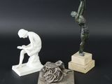 trois sculptures représentant un homme assis sur un bloc de bois