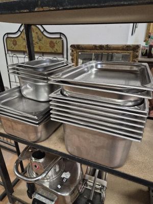 Plusieurs casseroles en acier inoxydable sont empilées sur une étagère dans une cuisine