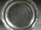 assiette en argent plaqué à bord festonné, posée sur un socle, sur un fond blanc