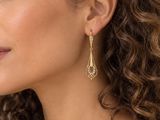 La femme porte une chemise blanche et des boucles d'oreilles dorées.