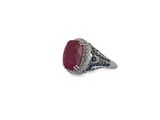a close up of a ring with a red stone surrounded by blue sapphires