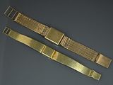 two pieces of gold metal bracelets on a gray surface