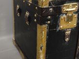 une malle noire et dorée posée sur une surface blanche