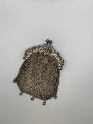 un porte-monnaie argenté entouré d'une chaîne, posé sur une surface blanche