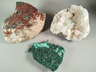 three pieces of green and red mineral on a white surface