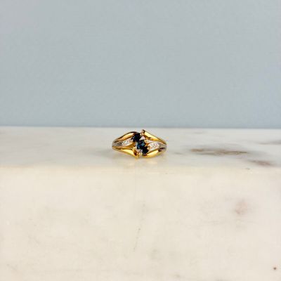 une image représentant une bague en or sertie d'une pierre bleue, posée sur une surface en marbre