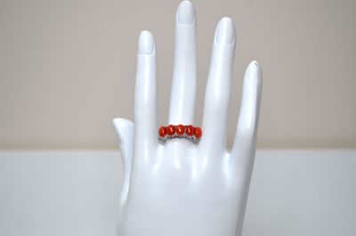 a white hand with a red beaded ring on it
