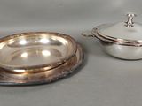 two silver dishes with lids on a table next to each other