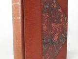 an old book with a red cover sitting on top of a white surface