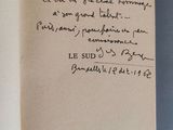 un livre ouvert, sur lequel est inscrit un poème manuscrit, posé sur une table