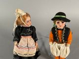 two porcelain dolls of children dressed in traditional clothing and hats