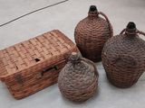 trois bouteilles en osier et un panier en osier posés sur une surface en béton