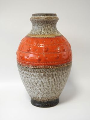 un vase orange et gris posé sur une surface blanche