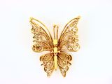 broche en forme de papillon doré aux ailes en filigrane sur fond blanc