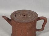 an old brown teapot with a wooden lid sitting on a white surface