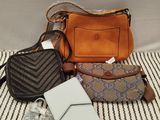 three purses and a wallet sitting on a bed with a striped blanket