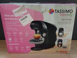 une machine à café encore dans son emballage, posée sur une table à côté d'une tasse de café