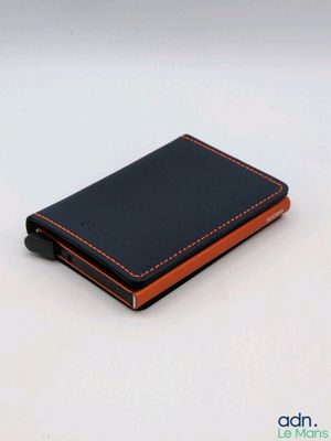 une photo d'un portefeuille noir et orange posé sur une surface blanche