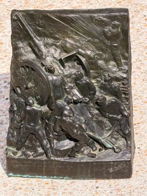 statue of a man with a sword and shield in front of a stone wall