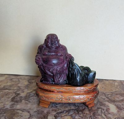 statue d'un Bouddha souriant, assis sur un socle en bois posé sur une surface en marbre