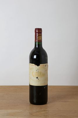 une bouteille de vin rouge posée sur une table en bois, avec un mur blanc en arrière-plan