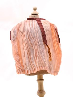 chemise plissée couleur pêche posée sur un mannequin, ornée d'un ruban rouge