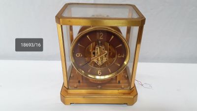 a gold clock with a glass case on a white table