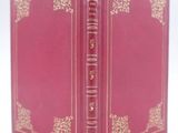 un vieux livre rouge avec des bordures dorées posé sur une surface blanche