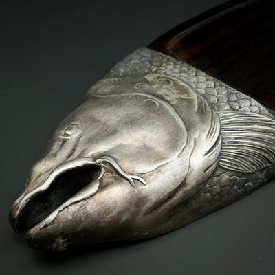 une tête de poisson argentée posée sur une cuillère en bois, sur une table